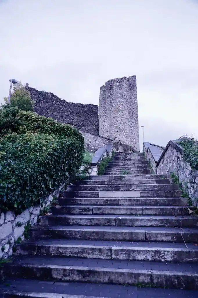 A wide-angle shot of a long, weathered stone staircase leading up to an ancient, partially ruined stone tower and wall under…