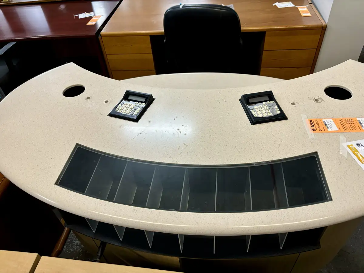 A curved beige countertop desk with two black calculators placed symmetrically on top, resembling eyes, and a long black…