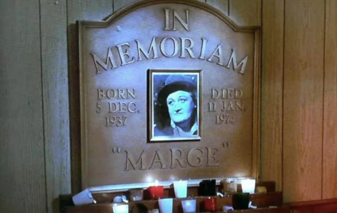 A wooden memorial plaque with engraved text reading 'IN MEMORIAM', birth and death dates (born 5 DEC. 1937, died 11 JAN…