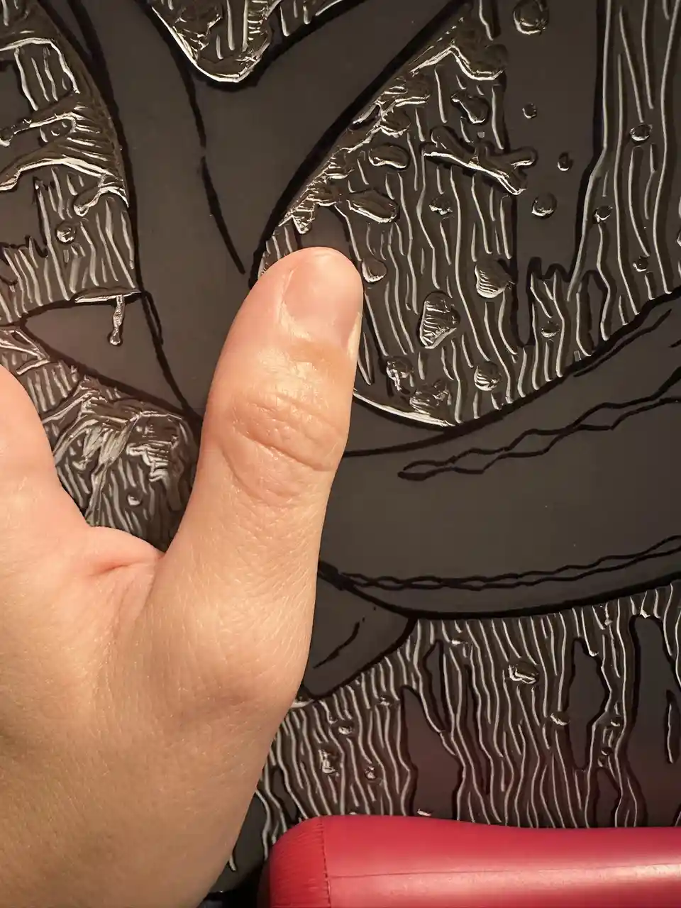 A close-up photo shows a person's thumb pointing at a black-and-white textured artwork that depicts a scene with bones and…