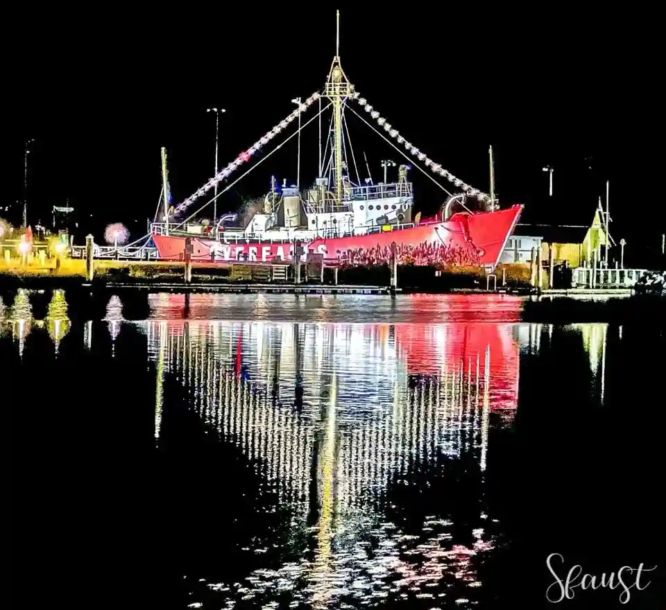 A red and white ship is docked at night, its hull and rigging illuminated, with the word 'SCREAMS' painted in large white…