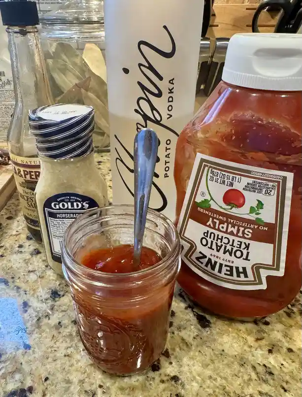 A kitchen counter displays a jar of mixed ketchup with a spoon, next to a large bottle of Heinz Simply Tomato Ketchup, a…