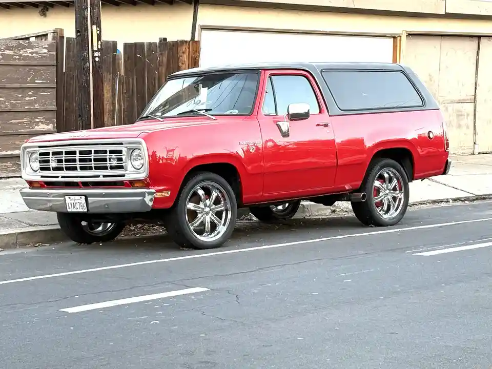 A red classic Chevrolet Blazer with a black roof is parked on a street, featuring shiny chrome wheels and a California…