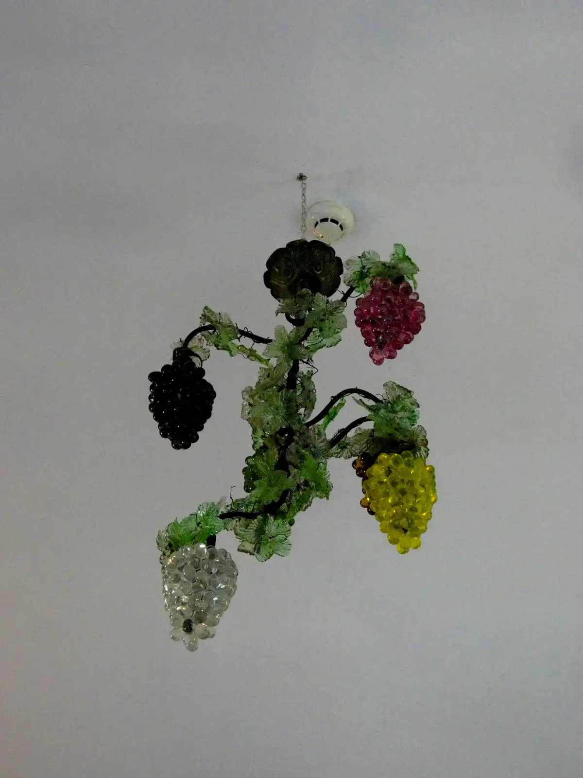 a decorative chandelier shaped like a grapevine with clusters of colorful glass grapes in black, pink, yellow, and clear…