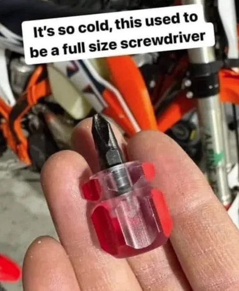 A hand holds a tiny, clear plastic screwdriver with a red grip and a small black bit, set against a blurred background of…