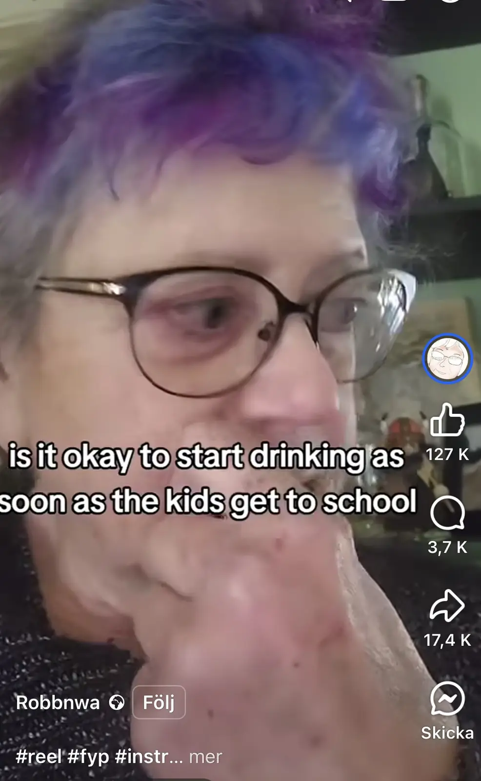 A close-up video of a person with short, purple and blue dyed hair and glasses, looking slightly to the side with a…