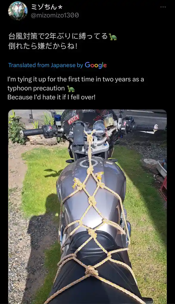 A dark gray motorcycle is secured with a crisscross pattern of thick, yellow rope tied around its fuel tank and seat, parked…
