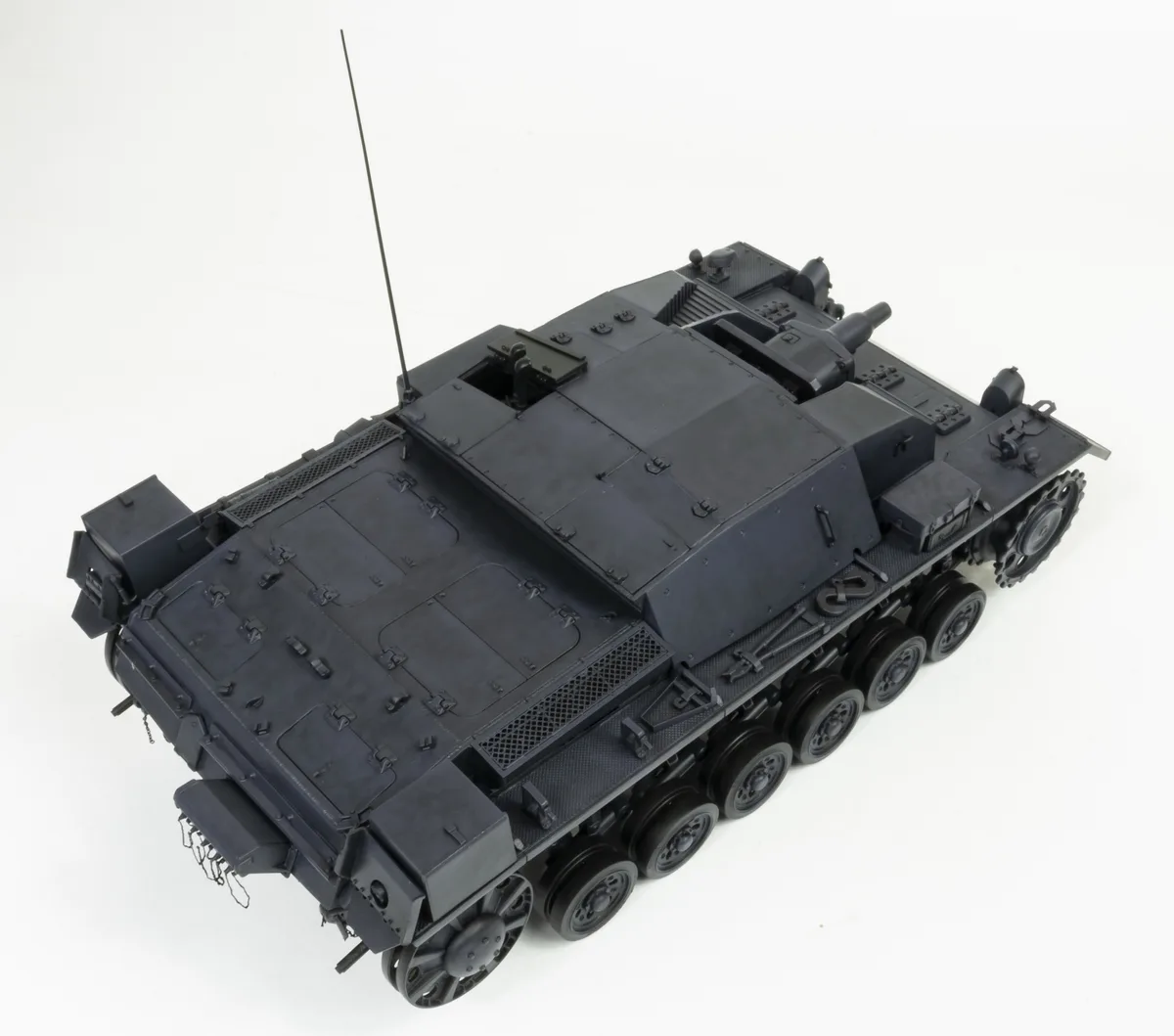 A detailed black model of a military tank with visible treads, gun barrel, antenna, and hatches, photographed against a…