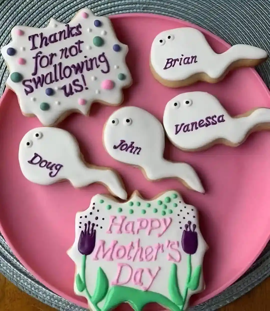 A pink plate holds several decorated sugar cookies: four shaped like tadpoles with names (Brian, Vanessa, John, Doug) and…