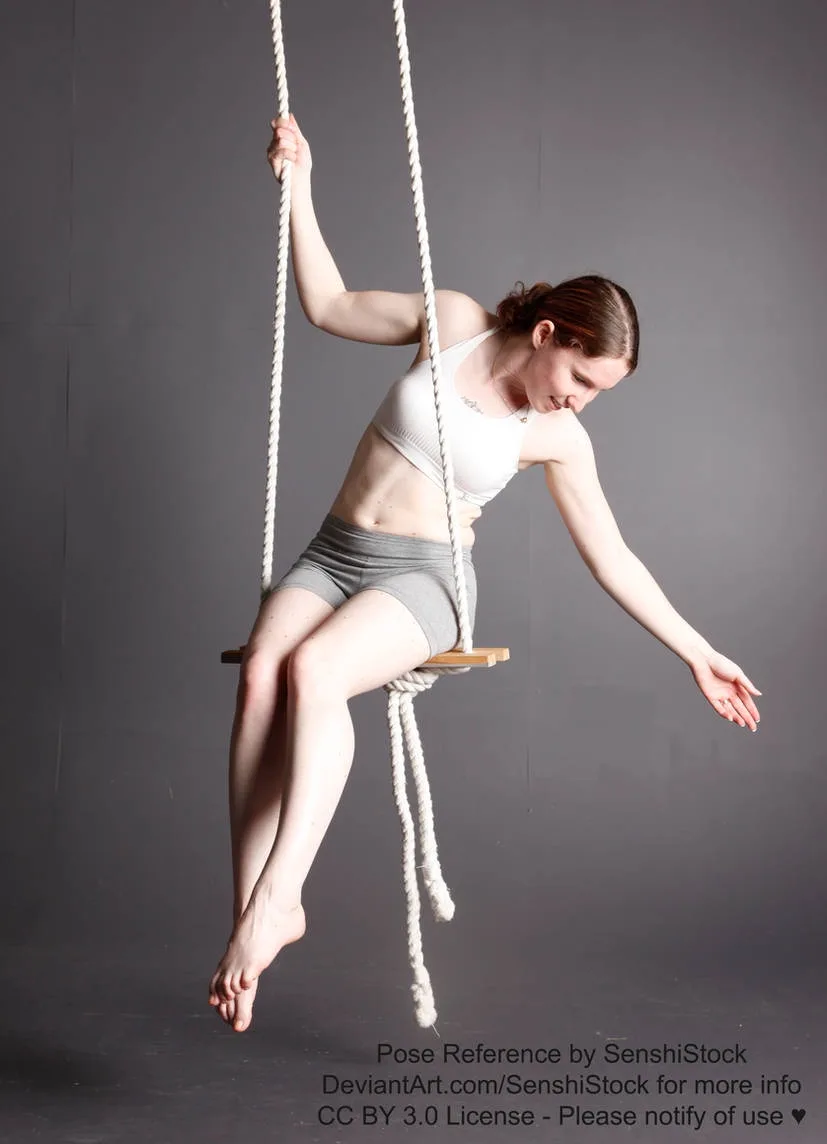 A woman in a white sports bra and gray shorts is suspended in a studio on a rope swing, her body arched gracefully as she…