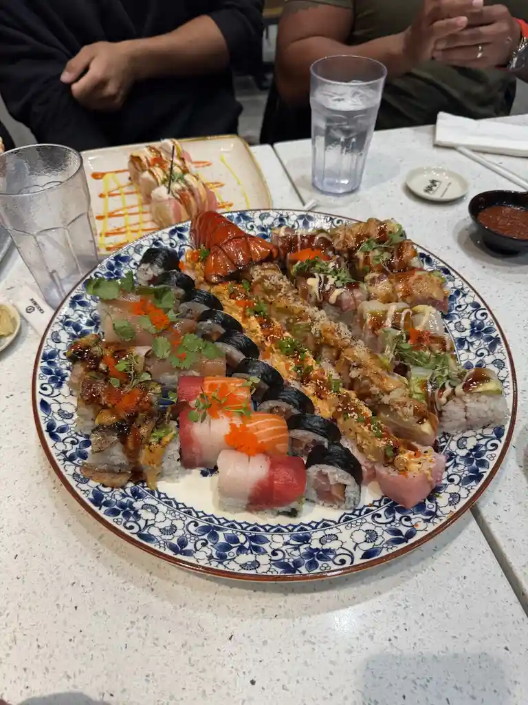 A large, ornate blue-and-white plate is filled with an assortment of sushi rolls and nigiri, including a prominent lobster…