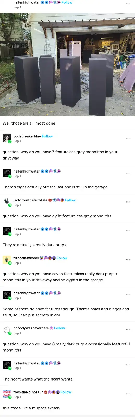 An image shows seven large, dark grey, featureless rectangular monoliths arranged in a driveway outside a garage. The…