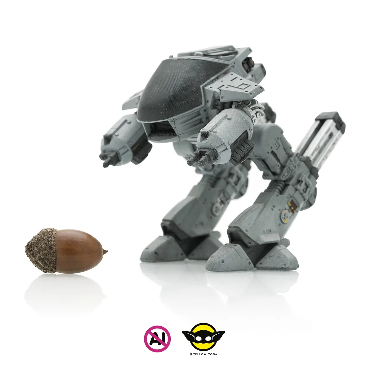 A detailed grey mech toy stands poised with weapons drawn, facing a single acorn on a reflective white surface. The mech…