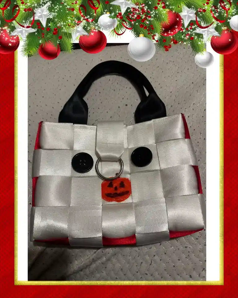 A woven white and red purse with black button eyes, a metal ring nose, and an orange felt jack-o'-lantern mouth, framed by a…