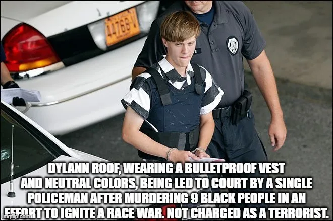A young man in a black-and-white striped shirt and a bulletproof vest is being escorted by a single police officer. He…