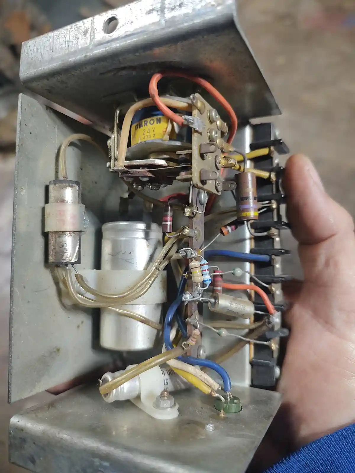 A close-up photo shows a hand holding open a metal electrical enclosure revealing a dense, messy tangle of wires, resistors…