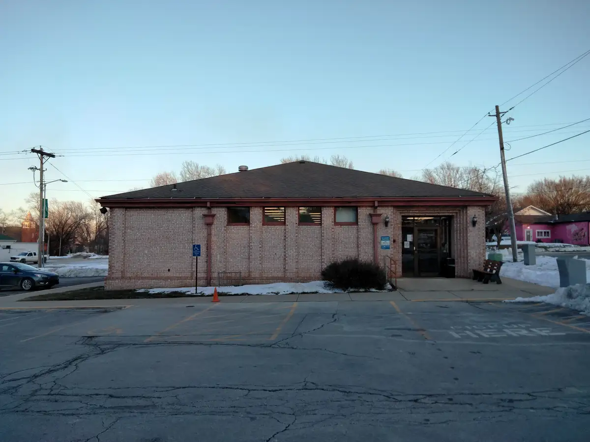 A photo of a small brick building with a parking lot in front, where the asphalt has "pick up here" painted in white…