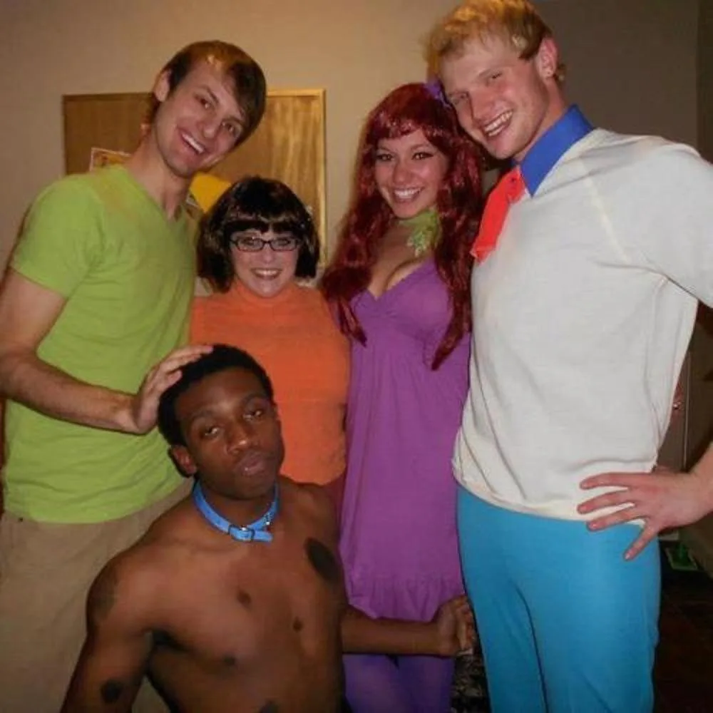 Five people dressed as Scooby-Doo characters pose for a photo; the person in the foreground is shirtless with a blue collar…
