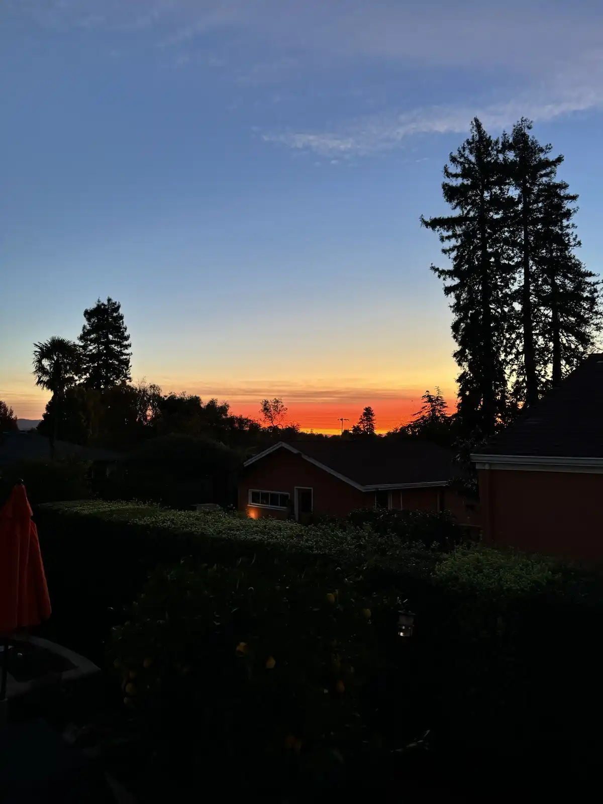 A serene sunset photo showing a residential backyard with silhouetted trees, a red house, and an orange umbrella, overlaid…