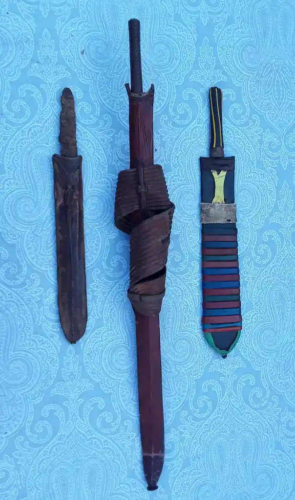 Three traditional knives or daggers with varying levels of decoration and wear are laid out vertically on a blue…