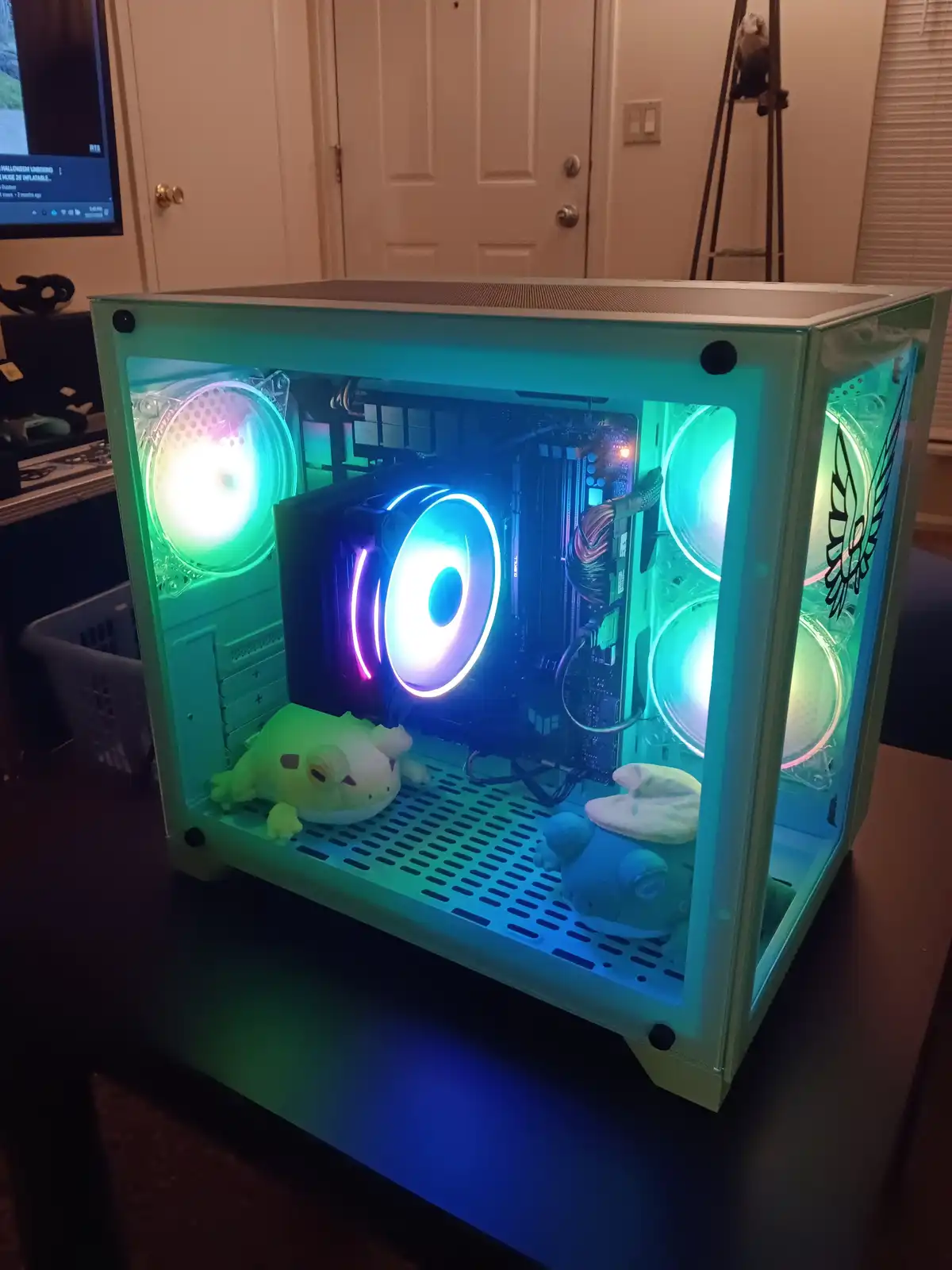 A custom-built computer case with transparent sides, glowing RGB fans, and visible internal components sits on a desk…