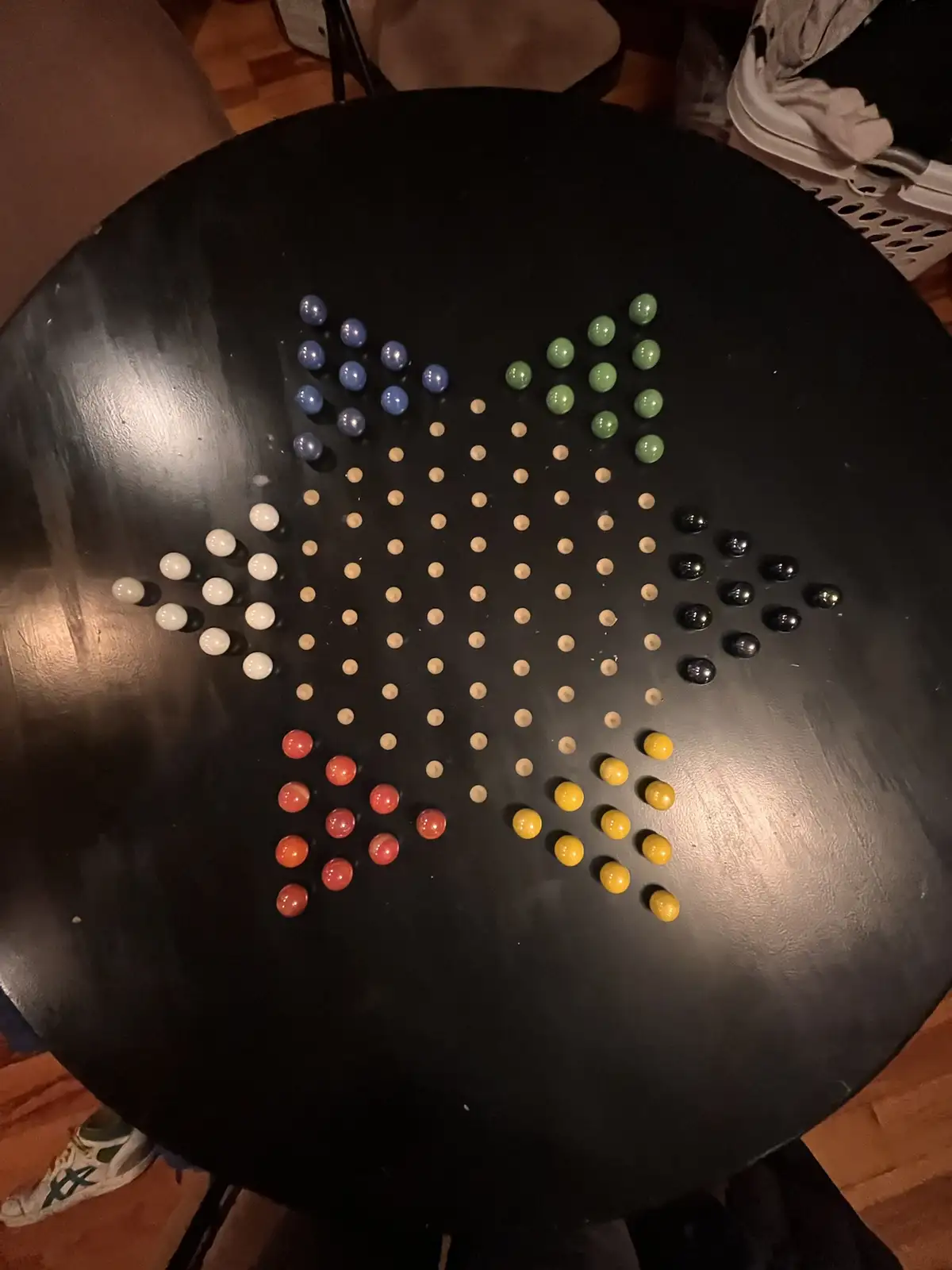A black circular table has a star shape formed by colorful marbles arranged on its surface. The star's points are made of…