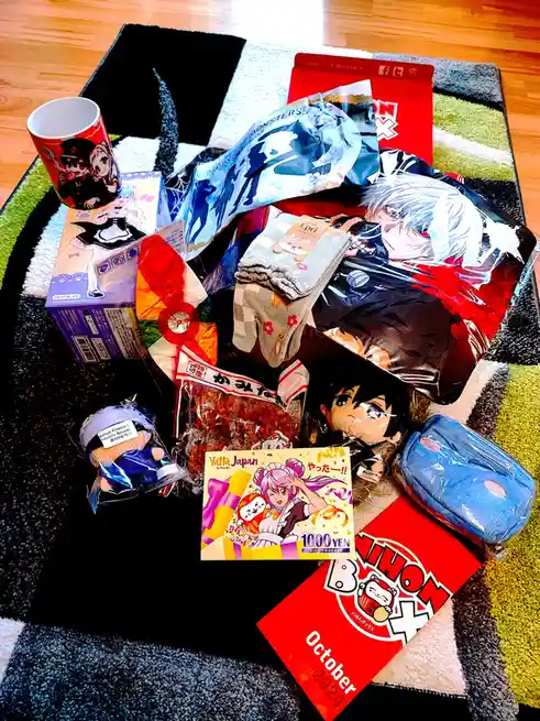 An overhead shot displays a colorful collection of anime merchandise spread across a patterned rug, including a mug…