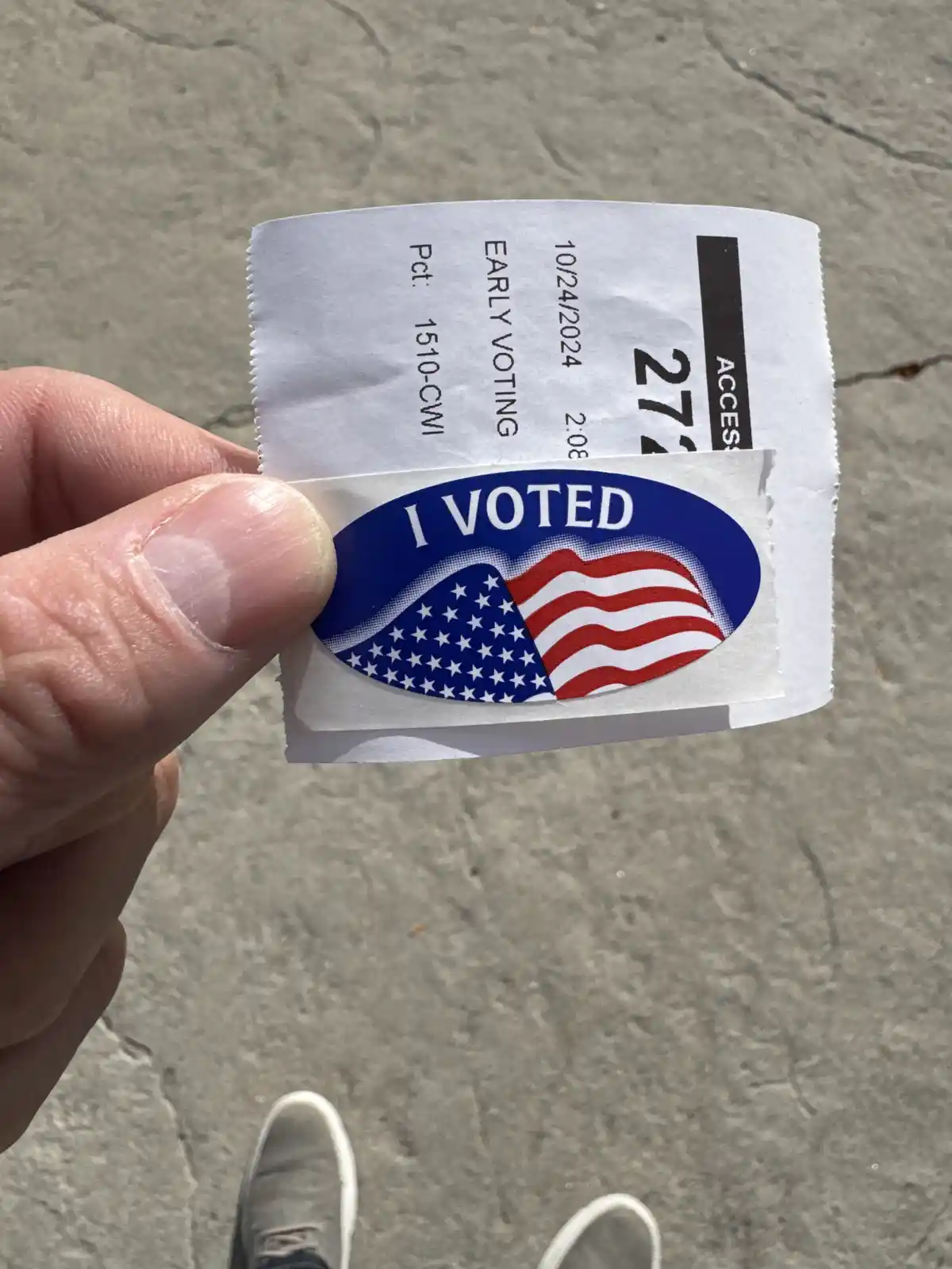 A hand holds up a paper early voting receipt from October 24, 2024, with an 'I VOTED' sticker featuring the American flag…
