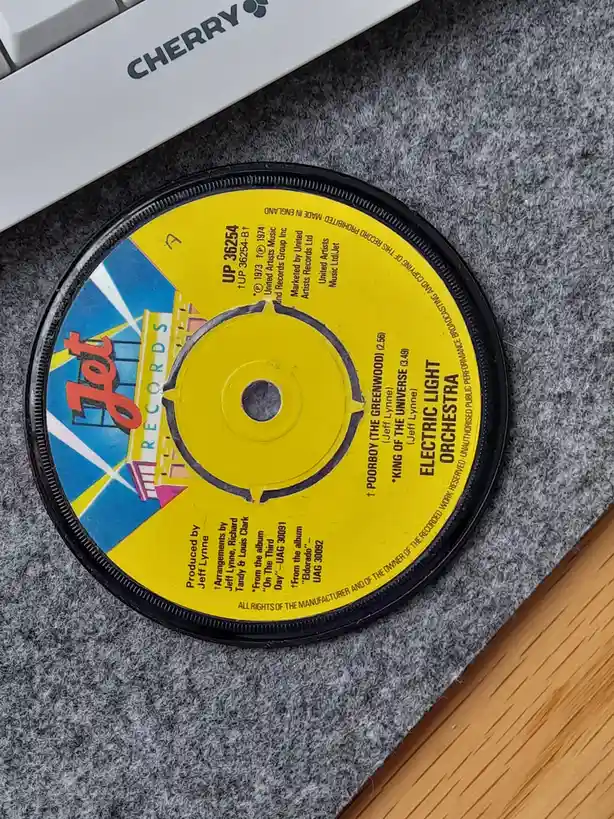 A close-up photo shows a yellow and blue 7-inch vinyl record label for 'Electric Light Orchestra' resting on grey fabric…