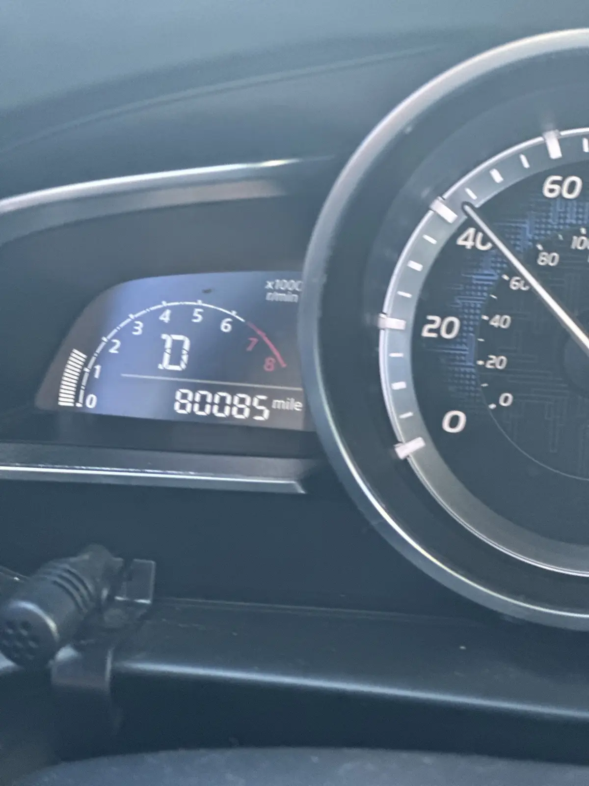 A close-up of a car's dashboard shows the odometer reading 80085 miles and the tachometer needle at 10,000 rpm (x1000…