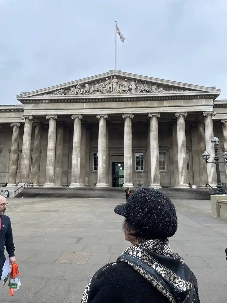 A person wearing a black hat and patterned scarf stands with their back to the camera, looking up at the grand, classical…
