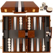 A wooden backgammon set with a brown and black checkered board, white and black checkers, dice, and dice cups, all arranged…