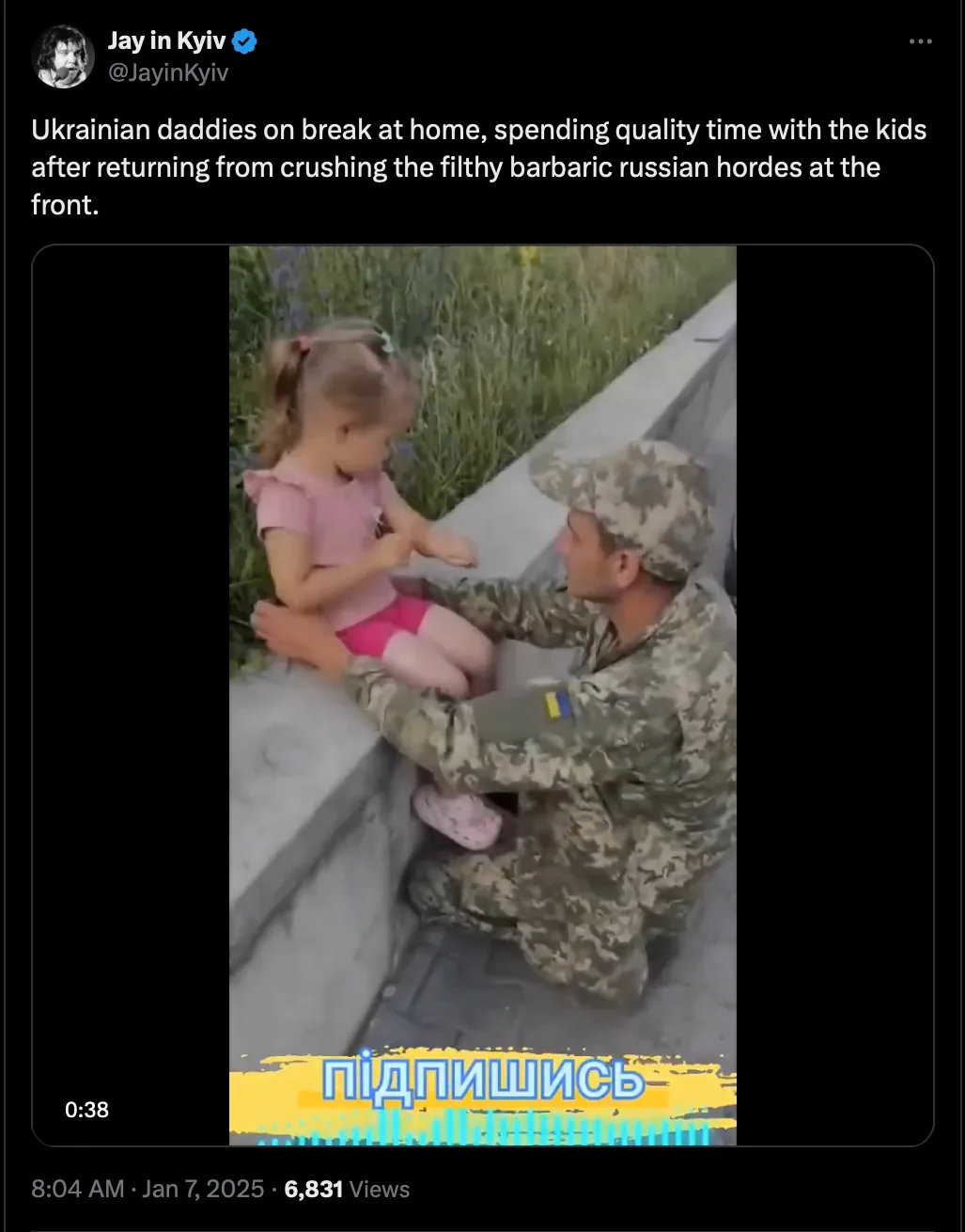 A man in Ukrainian military camouflage uniform kneels beside a young girl in a pink outfit, gently holding her hands as she…