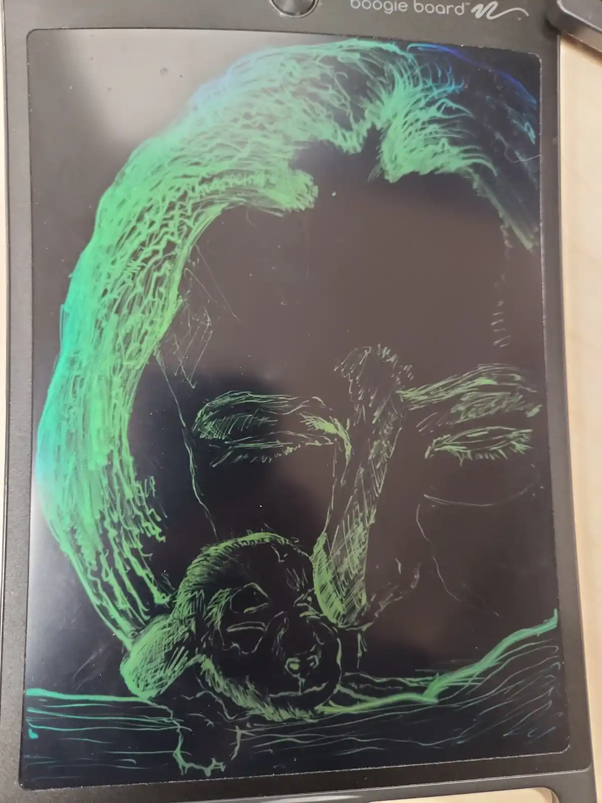 A green chalk-like drawing on a Boogie Board electronic drawing tablet depicts a person's face with a large wave crashing…
