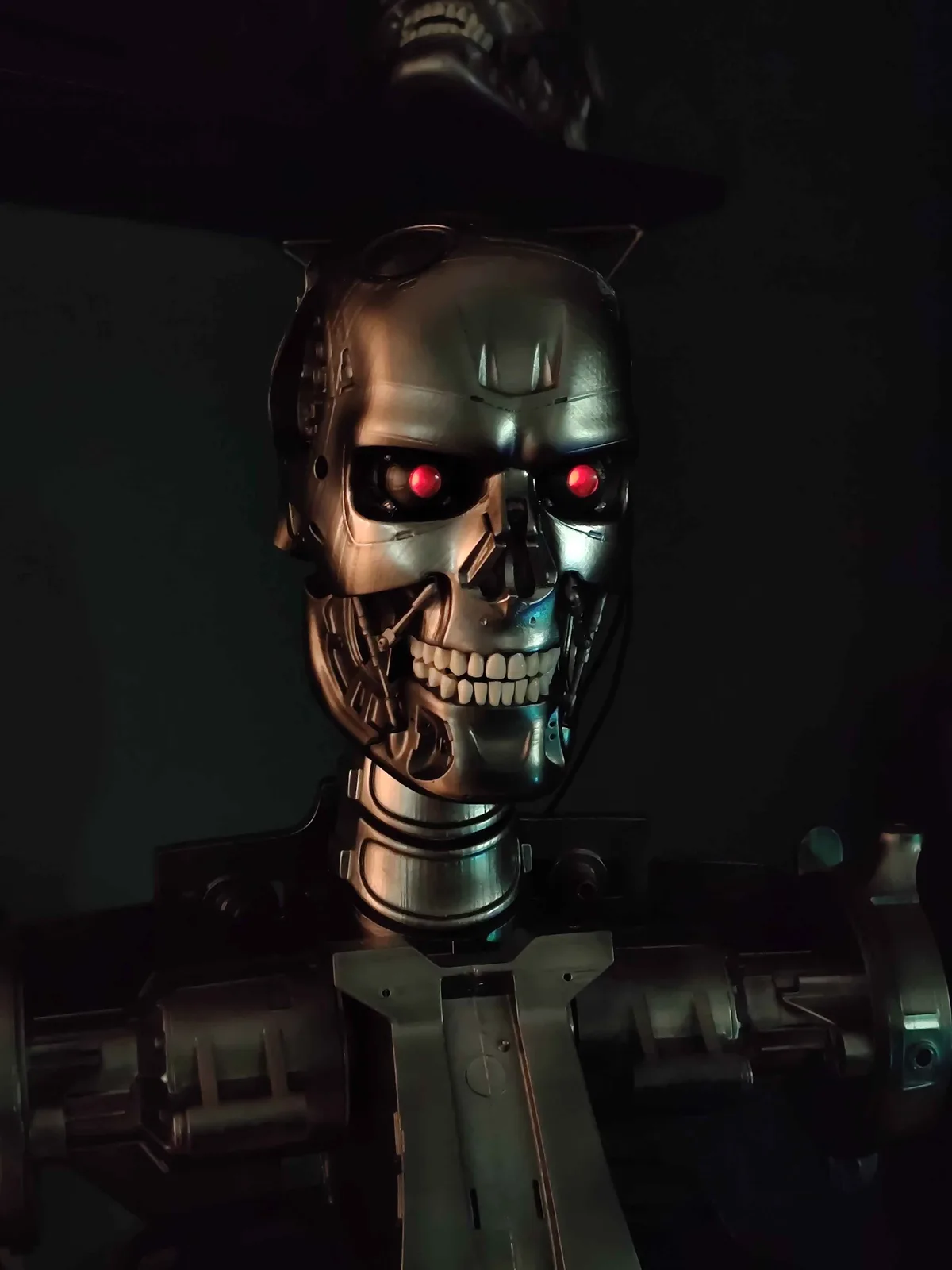 A close-up of a Terminator endoskeleton with glowing red eyes and a menacing grin, wearing a black top hat. The overlaid…