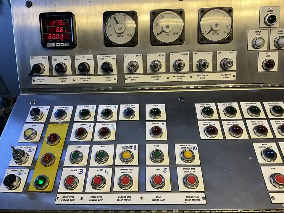 A close-up of a complex industrial control panel with numerous gauges, switches, and labeled buttons, including a digital…
