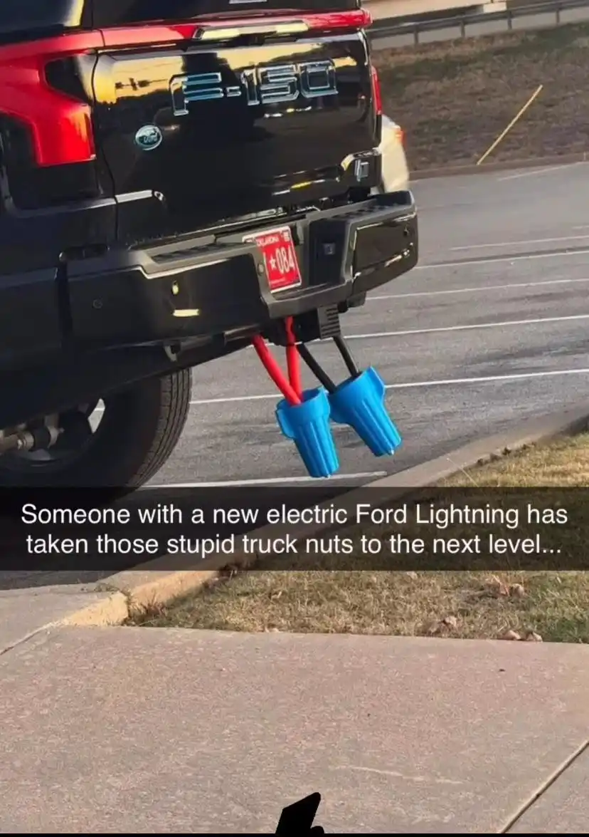 The image shows the rear of a black Ford F-150 truck parked in a lot, with its hitch holding two large blue electric vehicle…