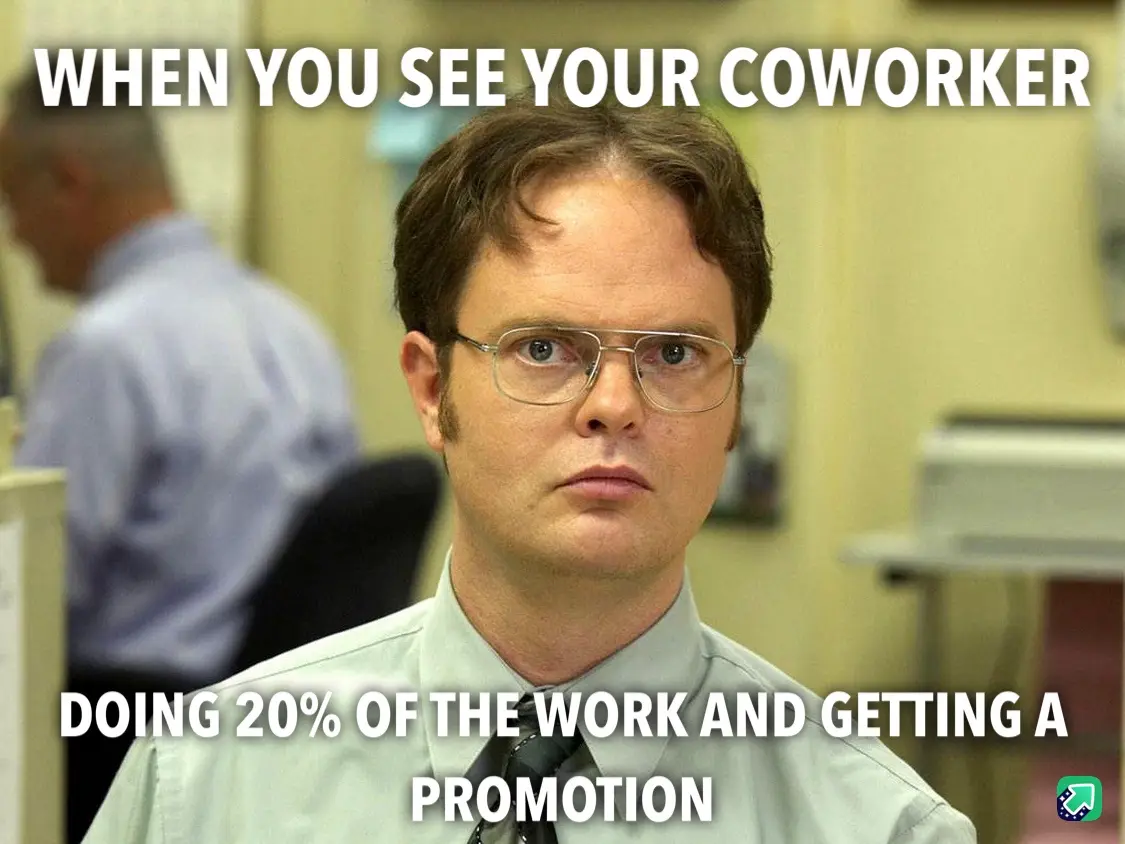 A man with glasses and a light-colored shirt stares intensely at the camera in an office setting, with another person…