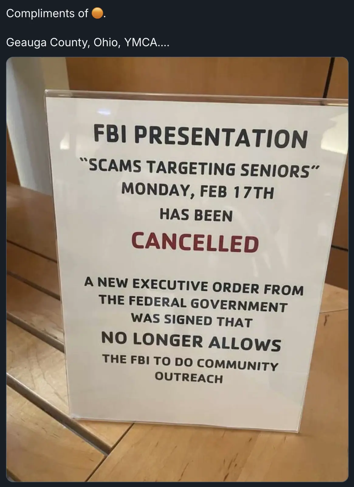 A white sign in a clear plastic stand on a wooden floor announces the cancellation of an 'FBI Presentation' about scams…