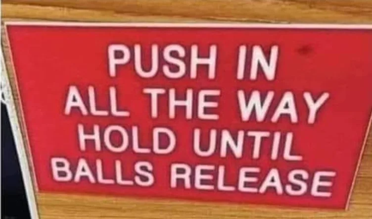 A red rectangular sign with white uppercase text instructs: 'PUSH IN ALL THE WAY HOLD UNTIL BALLS RELEASE'. The sign is…
