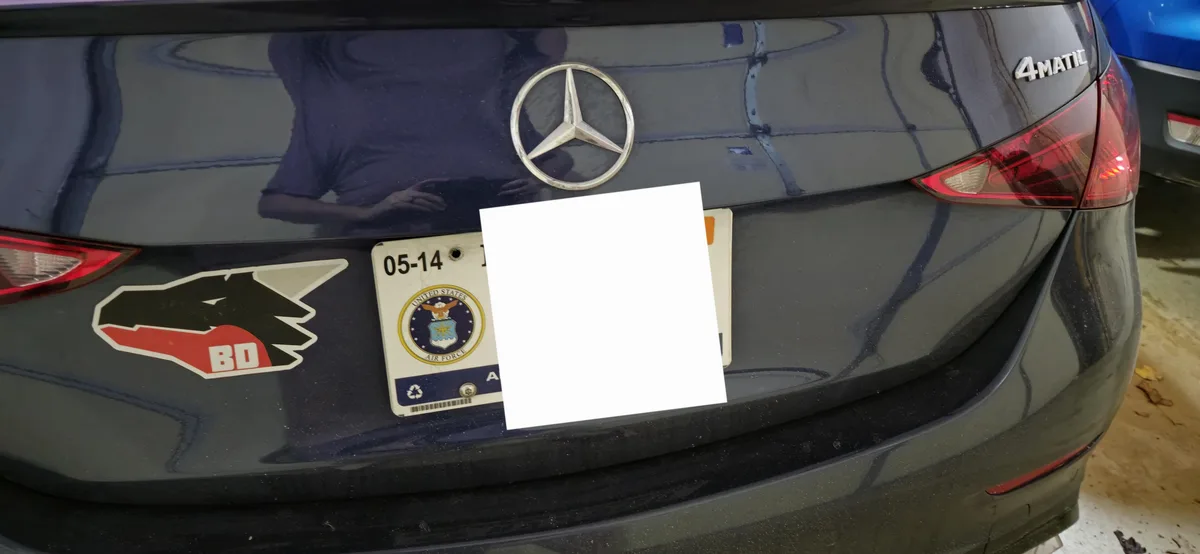 A close-up of the rear of a black Mercedes-Benz car with a white paper covering its license plate. The visible portion of…