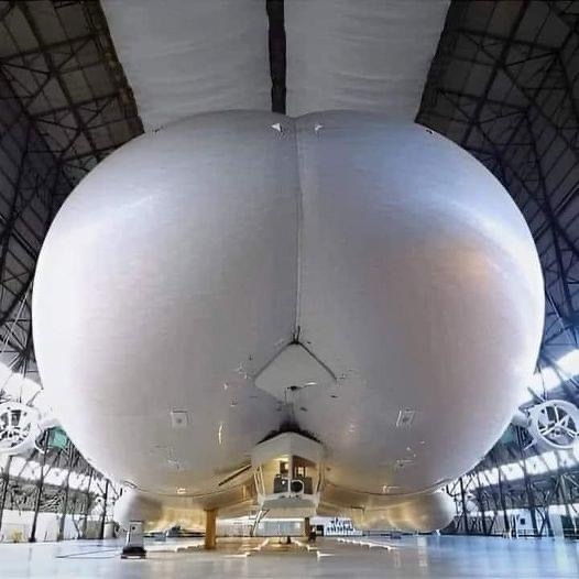 a large, white, spherical object resembling a human buttocks is shown from a low-angle perspective inside a vast industrial…