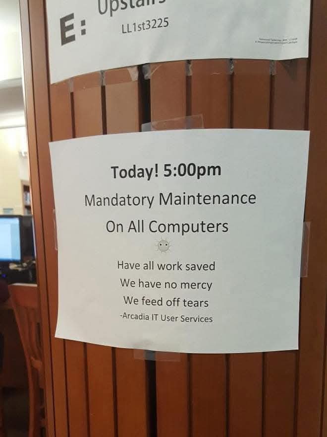 A white paper sign taped to a wooden door announces 'Today! 5:00pm Mandatory Maintenance On All Computers' with a small sad…
