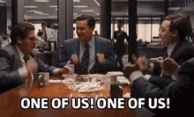 Six identical frames show three men in suits sitting around a conference table, all shouting the phrase 'ONE OF US! ONE OF…