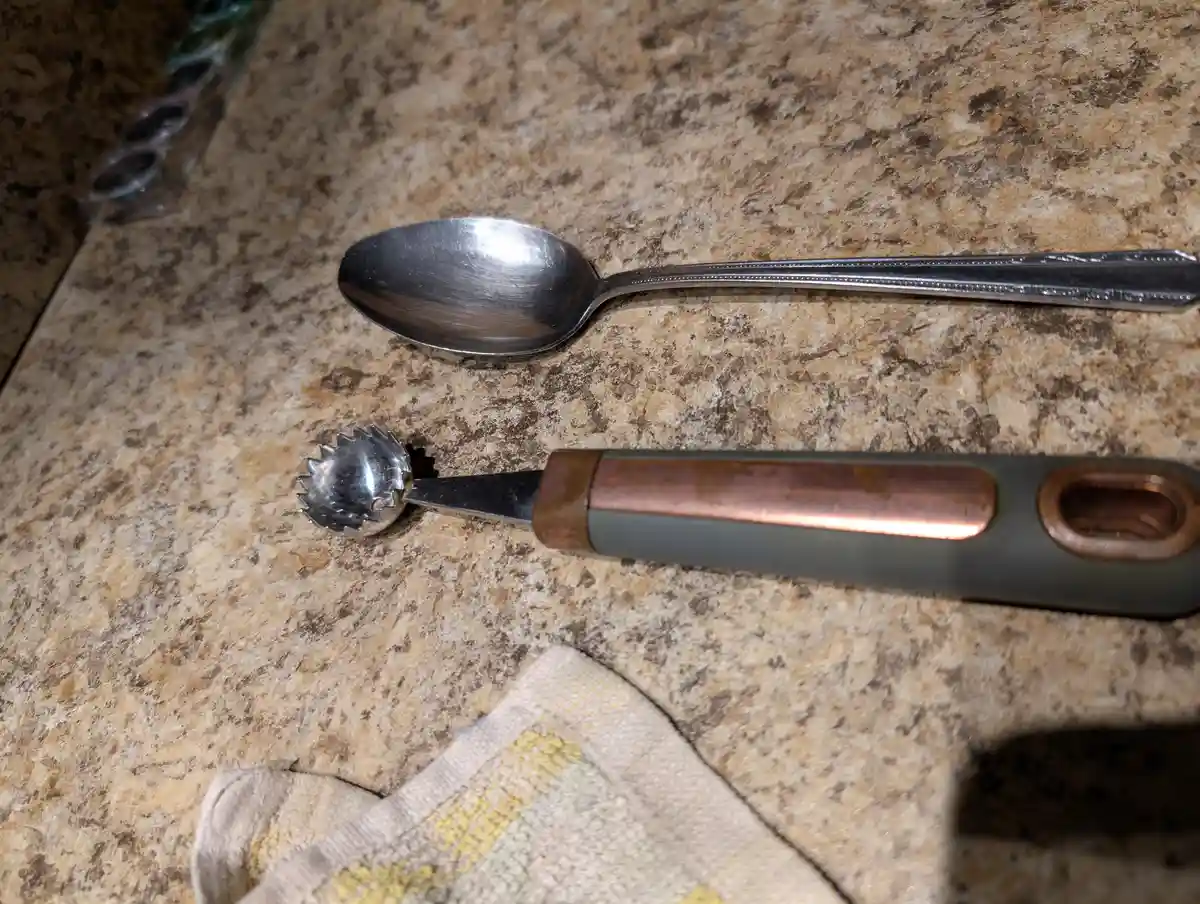 A close-up photo shows a standard metal spoon and a broken ice cream scoop lying side-by-side on a speckled granite…