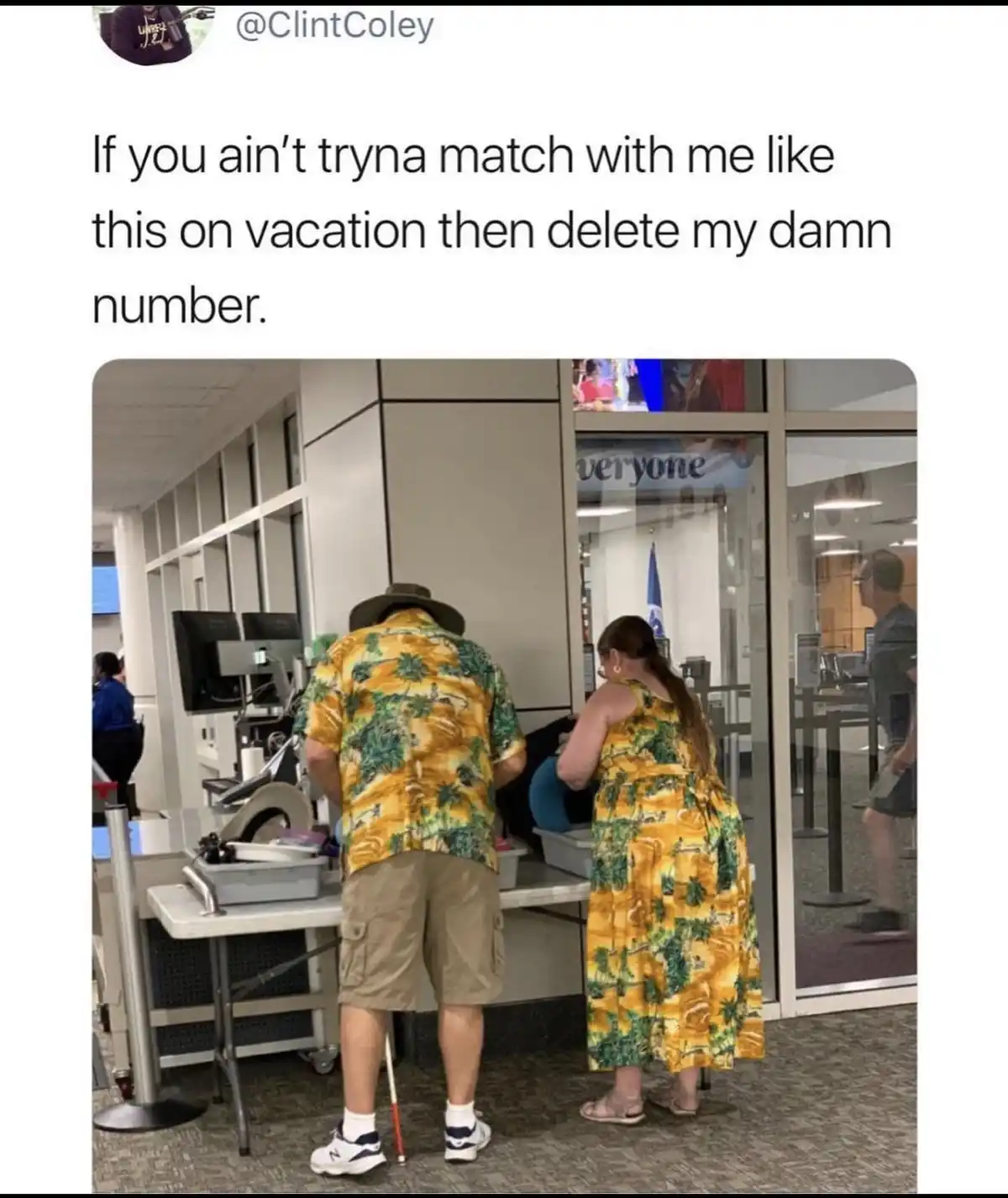 A man and woman, both wearing matching yellow and green tropical print shirts and shorts/dress, stand at an airport security…