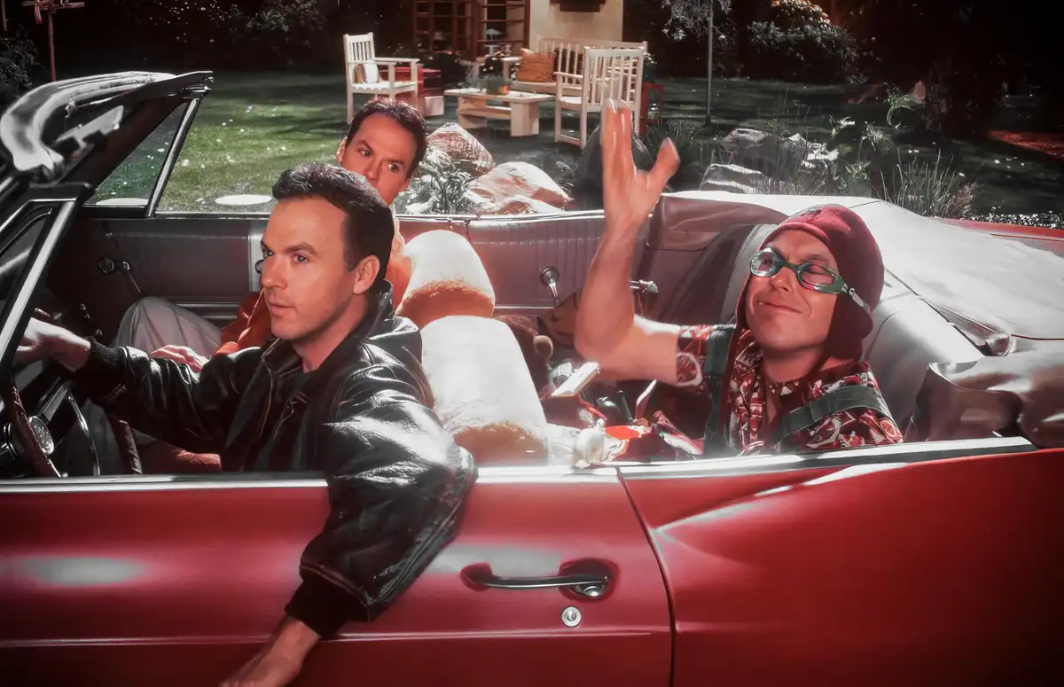 Three men are in a red convertible car at night; the driver looks serious, the passenger in the back has a shocked…
