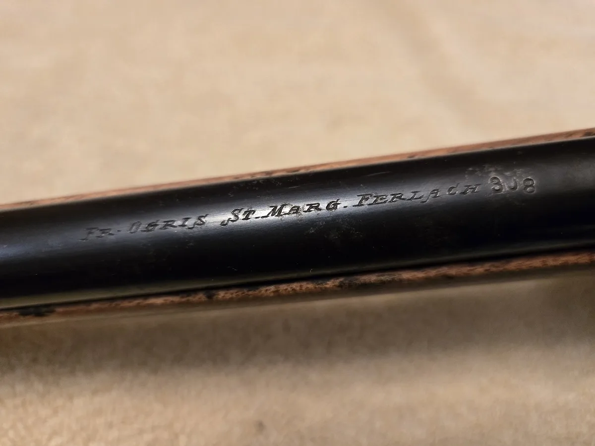 A close-up photo shows the engraved text 'FR. OGRIS ST. MARG. FERLACH 3J8' on a black metal barrel, likely from a rifle or…