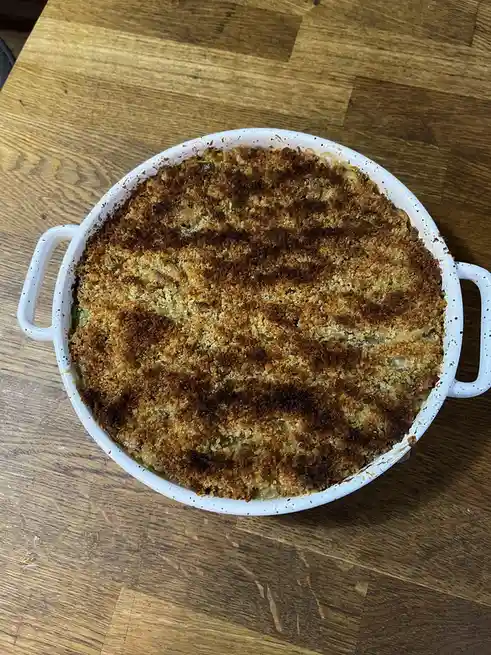 A top-down photo of a white speckled ceramic baking dish with two handles, sitting on a wooden table. The dish contains a…