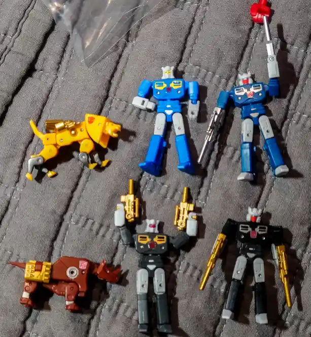 Six small toy figures, including two blue robot figures, one black robot figure, one yellow dog-like robot, and one brown…